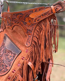 Close-up of a brown leather saddle with intricate patterns and fringes.